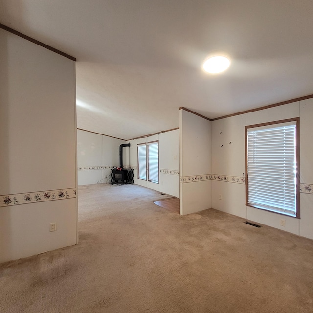 carpeted empty room with ornamental molding and a wood stove