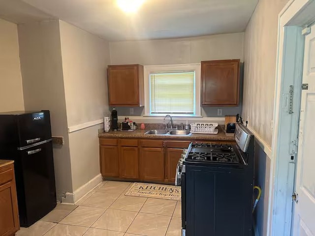 kitchen with stainless steel range with gas cooktop, black refrigerator, sink, and light tile patterned floors