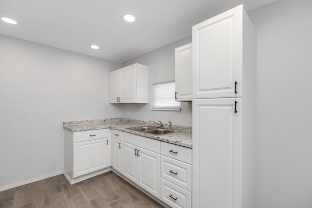 kitchen with white cabinetry, sink, and light stone countertops