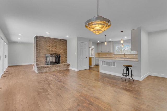 unfurnished living room featuring a brick fireplace, sink, and light hardwood / wood-style floors