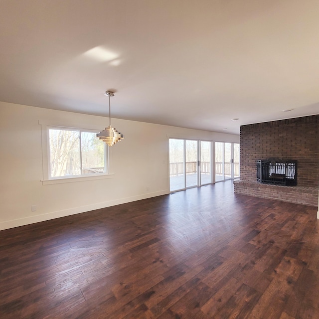 unfurnished living room featuring dark hardwood / wood-style floors, a chandelier, and a brick fireplace