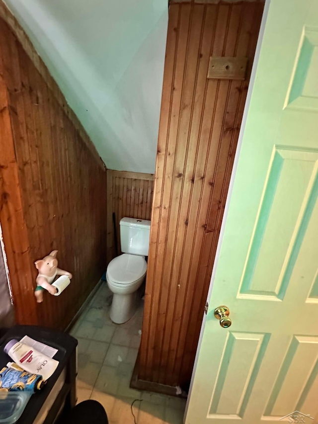 bathroom featuring tile patterned flooring, vaulted ceiling, toilet, and wood walls