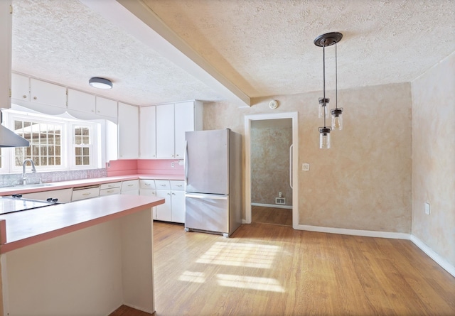 kitchen featuring sink, white cabinetry, decorative light fixtures, light hardwood / wood-style flooring, and stainless steel fridge