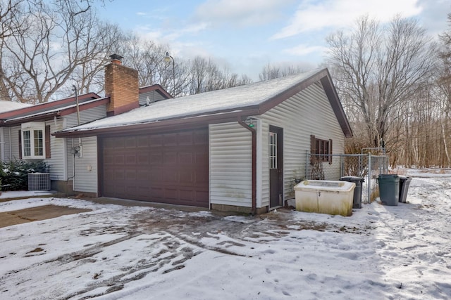 view of snowy exterior with a garage and central AC unit