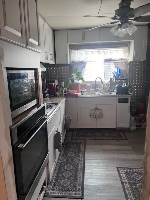 kitchen with sink, ceiling fan, stainless steel appliances, light hardwood / wood-style floors, and white cabinets