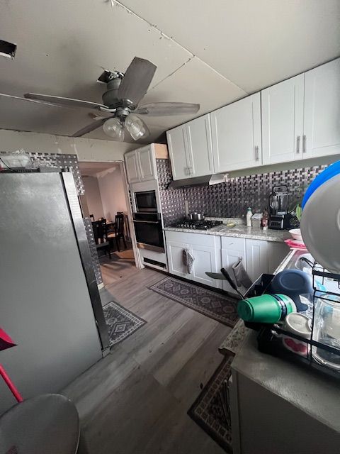 kitchen with built in microwave, light hardwood / wood-style flooring, oven, decorative backsplash, and white cabinets