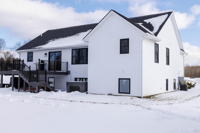 snow covered back of property with cooling unit and a deck