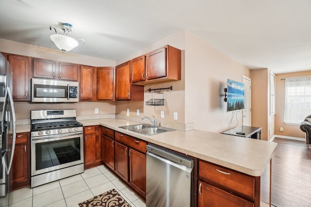 kitchen with brown cabinets, light countertops, appliances with stainless steel finishes, a sink, and a peninsula