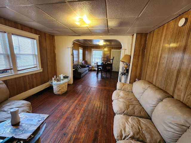 living room with a wealth of natural light, wooden walls, dark hardwood / wood-style floors, and a paneled ceiling