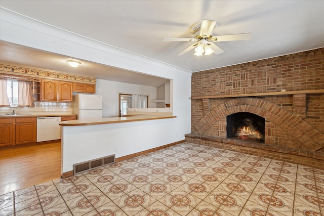 unfurnished living room with a brick fireplace, crown molding, sink, and ceiling fan