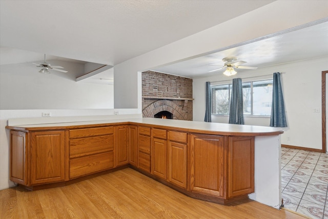 kitchen featuring ceiling fan, a brick fireplace, light hardwood / wood-style floors, and kitchen peninsula