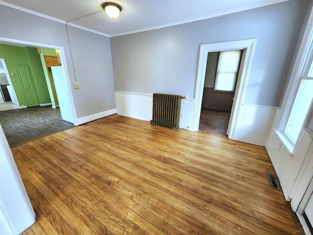 empty room with ornamental molding, a healthy amount of sunlight, radiator heating unit, and light hardwood / wood-style floors