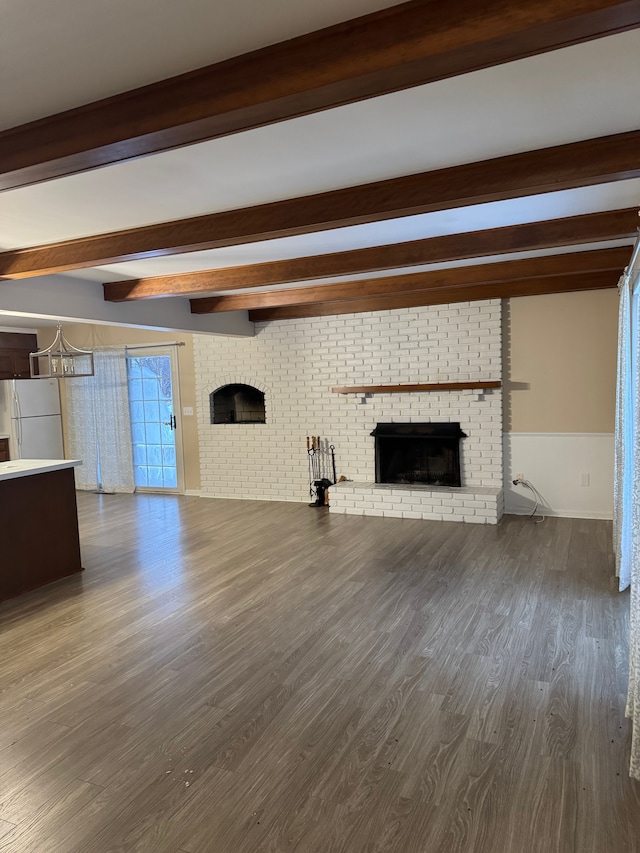 unfurnished living room with beamed ceiling, hardwood / wood-style floors, and a brick fireplace