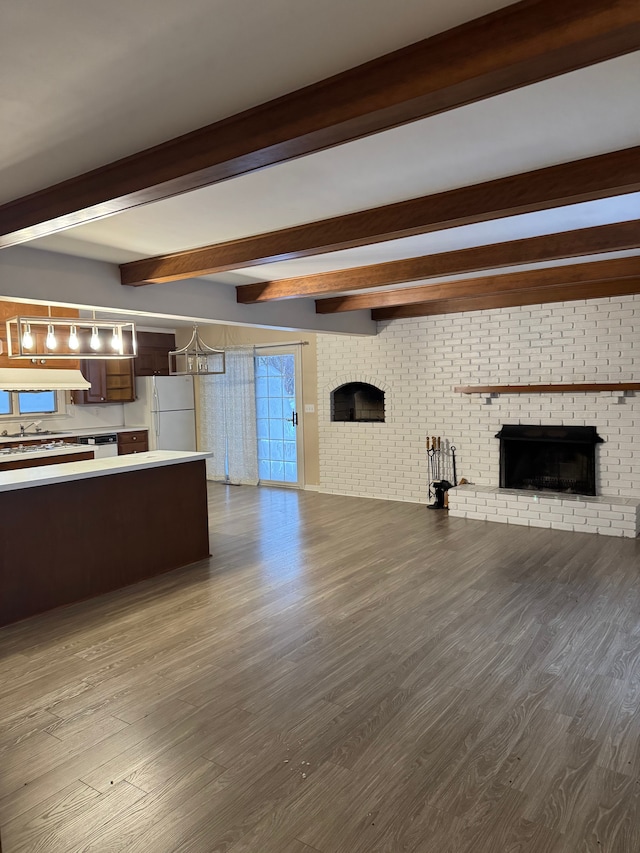 unfurnished living room featuring beamed ceiling, wood-type flooring, a brick fireplace, and brick wall