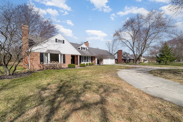 view of front of home with a chimney, driveway, brick siding, a front yard, and a garage