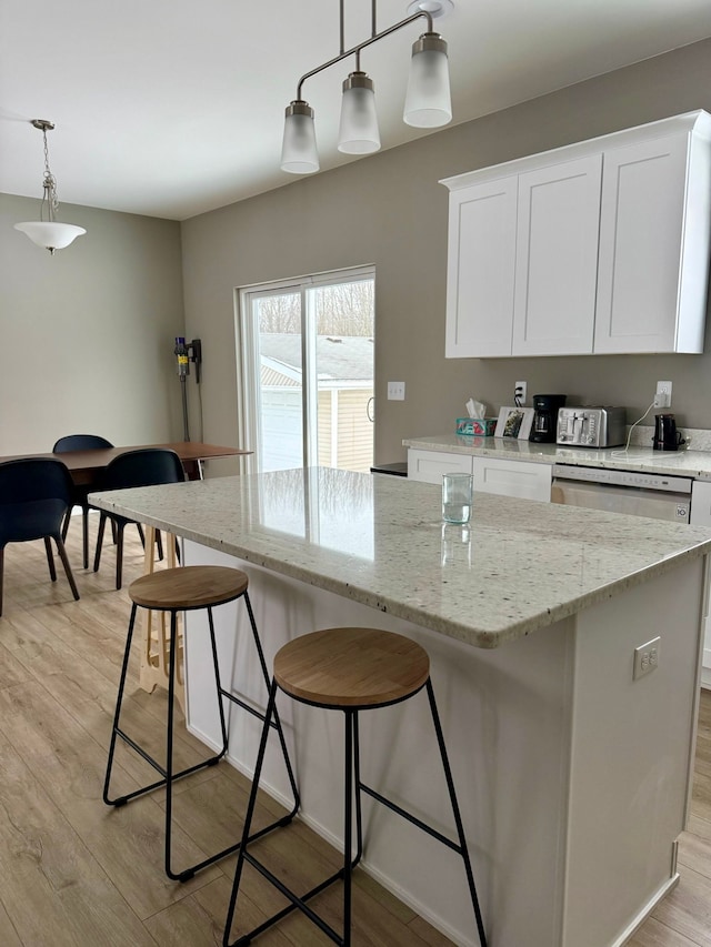 kitchen featuring white cabinetry, a center island, hanging light fixtures, light wood-type flooring, and light stone countertops