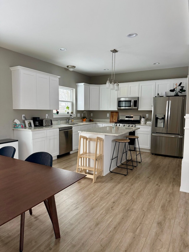 kitchen featuring white cabinetry, appliances with stainless steel finishes, a center island, and decorative light fixtures