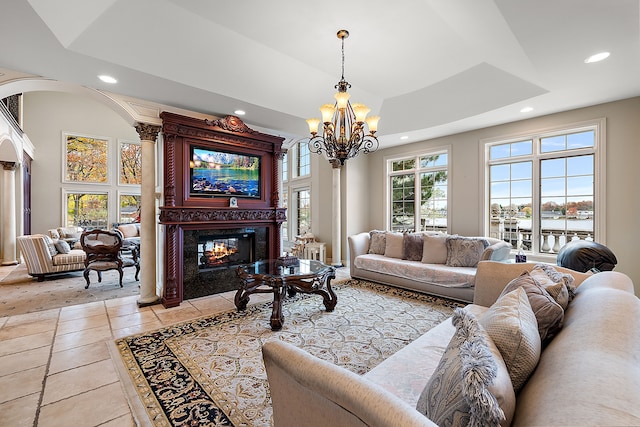 tiled living room with a raised ceiling, an inviting chandelier, a fireplace, and ornate columns