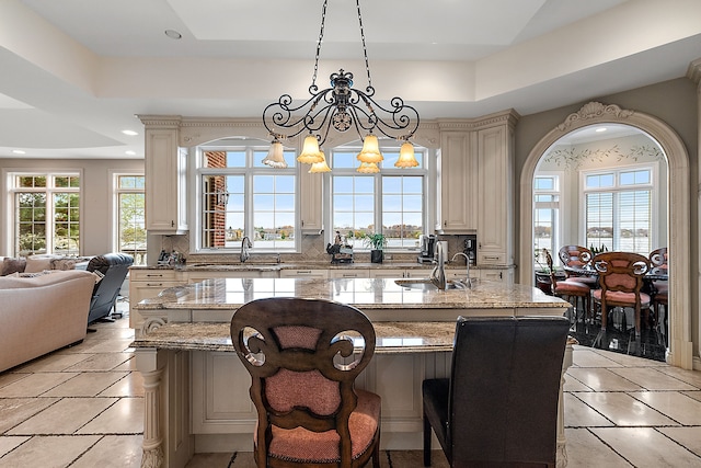 kitchen featuring light stone counters, open floor plan, a center island, pendant lighting, and a sink