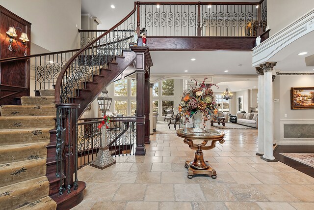 entryway with decorative columns, crown molding, a towering ceiling, and a notable chandelier