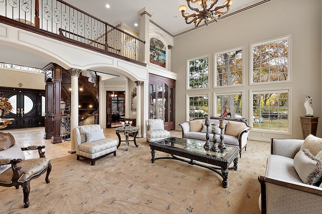 living room with french doors, an inviting chandelier, ornamental molding, a towering ceiling, and decorative columns