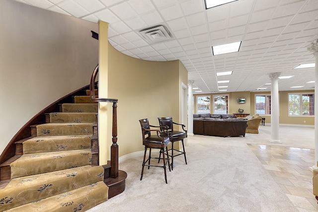 interior space featuring a drop ceiling, carpet floors, visible vents, baseboards, and decorative columns