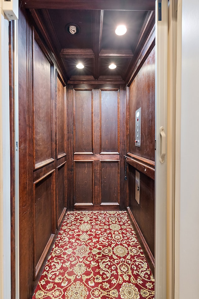 interior details featuring carpet, crown molding, elevator, wood walls, and coffered ceiling