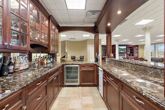 bar featuring a dry bar, a paneled ceiling, stone tile flooring, a glass covered fireplace, and beverage cooler