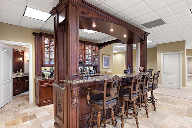 bar with light stone countertops and a drop ceiling