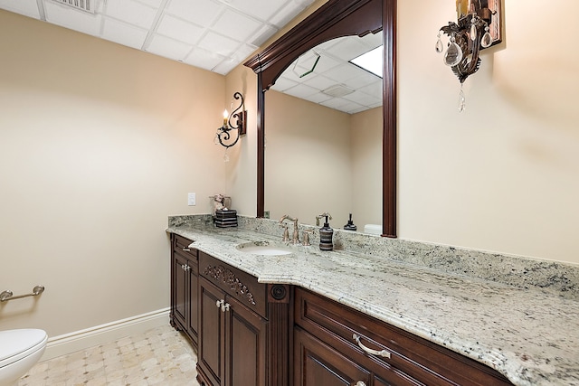 bathroom with toilet, vanity, a drop ceiling, baseboards, and tile patterned floors