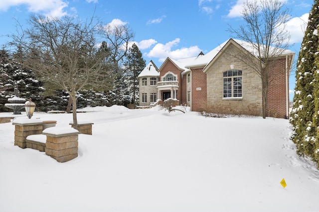 snow covered rear of property with stone siding and brick siding