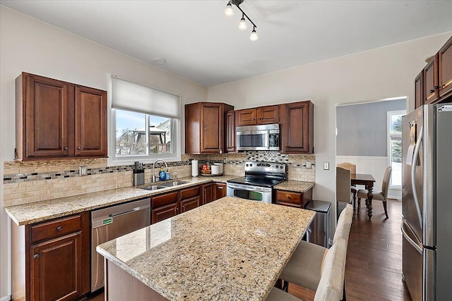 kitchen with sink, a breakfast bar area, stainless steel appliances, light stone counters, and a kitchen island