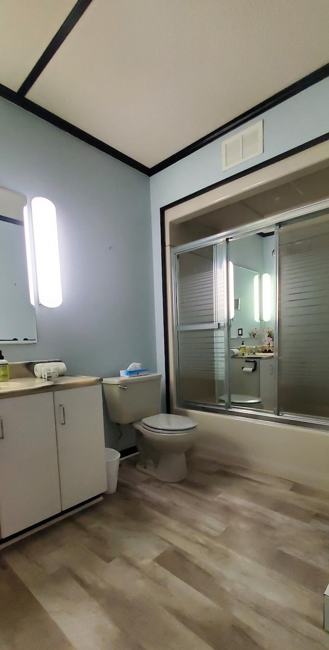 full bathroom with combined bath / shower with glass door, wood-type flooring, vanity, ornamental molding, and toilet