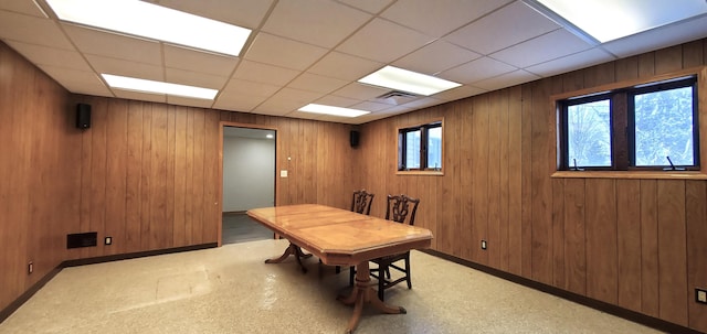 dining room with a paneled ceiling and wood walls