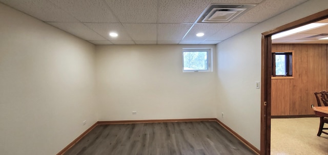 basement featuring hardwood / wood-style floors, a paneled ceiling, and wood walls