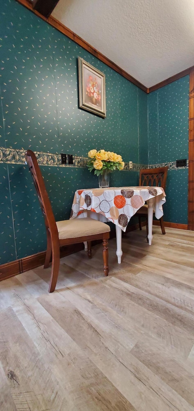 dining area with wood-type flooring, ornamental molding, and a textured ceiling