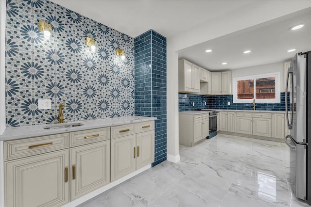 kitchen with sink, tasteful backsplash, light stone counters, appliances with stainless steel finishes, and cream cabinetry