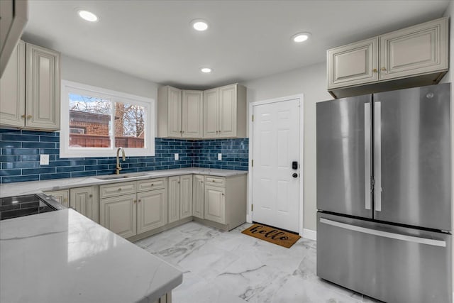 kitchen with tasteful backsplash, stainless steel fridge, sink, and light stone counters