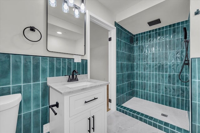 bathroom with tile walls, vanity, toilet, and tiled shower