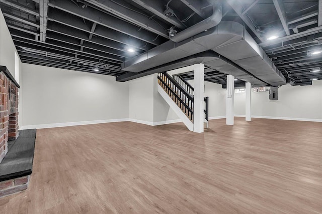 basement featuring hardwood / wood-style flooring, a brick fireplace, and electric panel