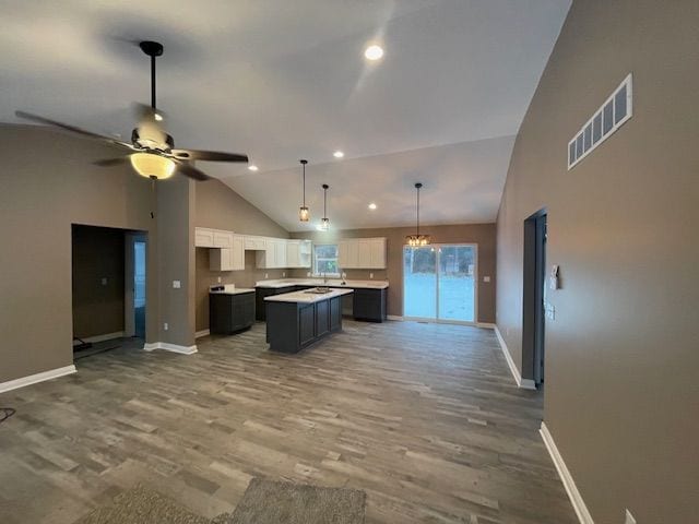 kitchen with lofted ceiling, white cabinetry, wood-type flooring, a kitchen island, and ceiling fan with notable chandelier