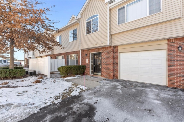 snow covered property featuring central AC and a garage