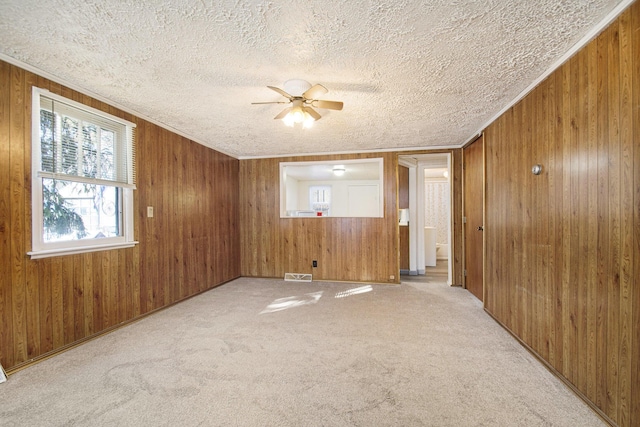 carpeted empty room featuring ceiling fan, a textured ceiling, and wood walls