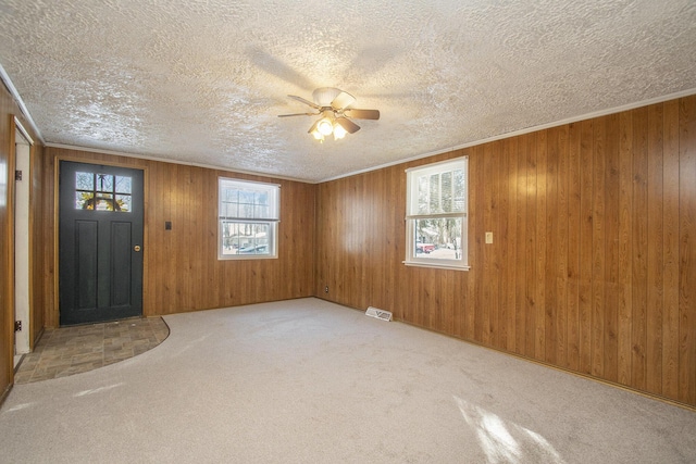 carpeted entryway with a textured ceiling, ceiling fan, and wood walls