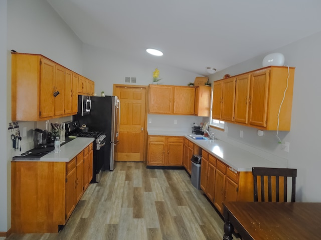 kitchen with lofted ceiling, sink, light hardwood / wood-style flooring, and stainless steel gas stove