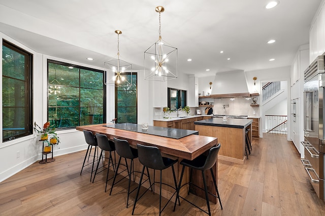 kitchen with premium range hood, white cabinetry, decorative light fixtures, a center island, and light hardwood / wood-style flooring