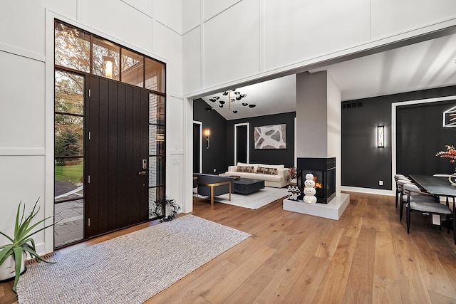 foyer entrance with a high ceiling, a multi sided fireplace, and light hardwood / wood-style floors