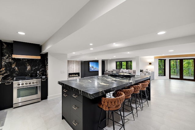 kitchen featuring stainless steel stove, a kitchen breakfast bar, decorative backsplash, a large island, and wall chimney range hood