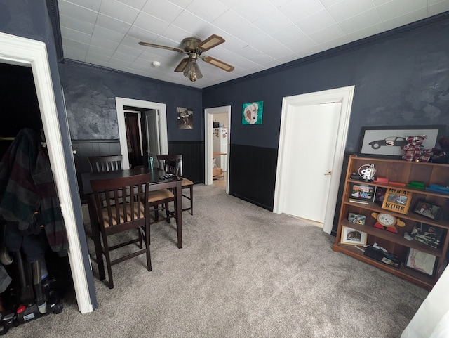 carpeted dining room with ornamental molding and ceiling fan