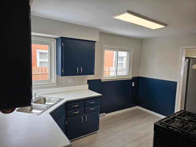 kitchen with blue cabinetry, sink, black range with gas stovetop, stainless steel fridge, and light hardwood / wood-style floors